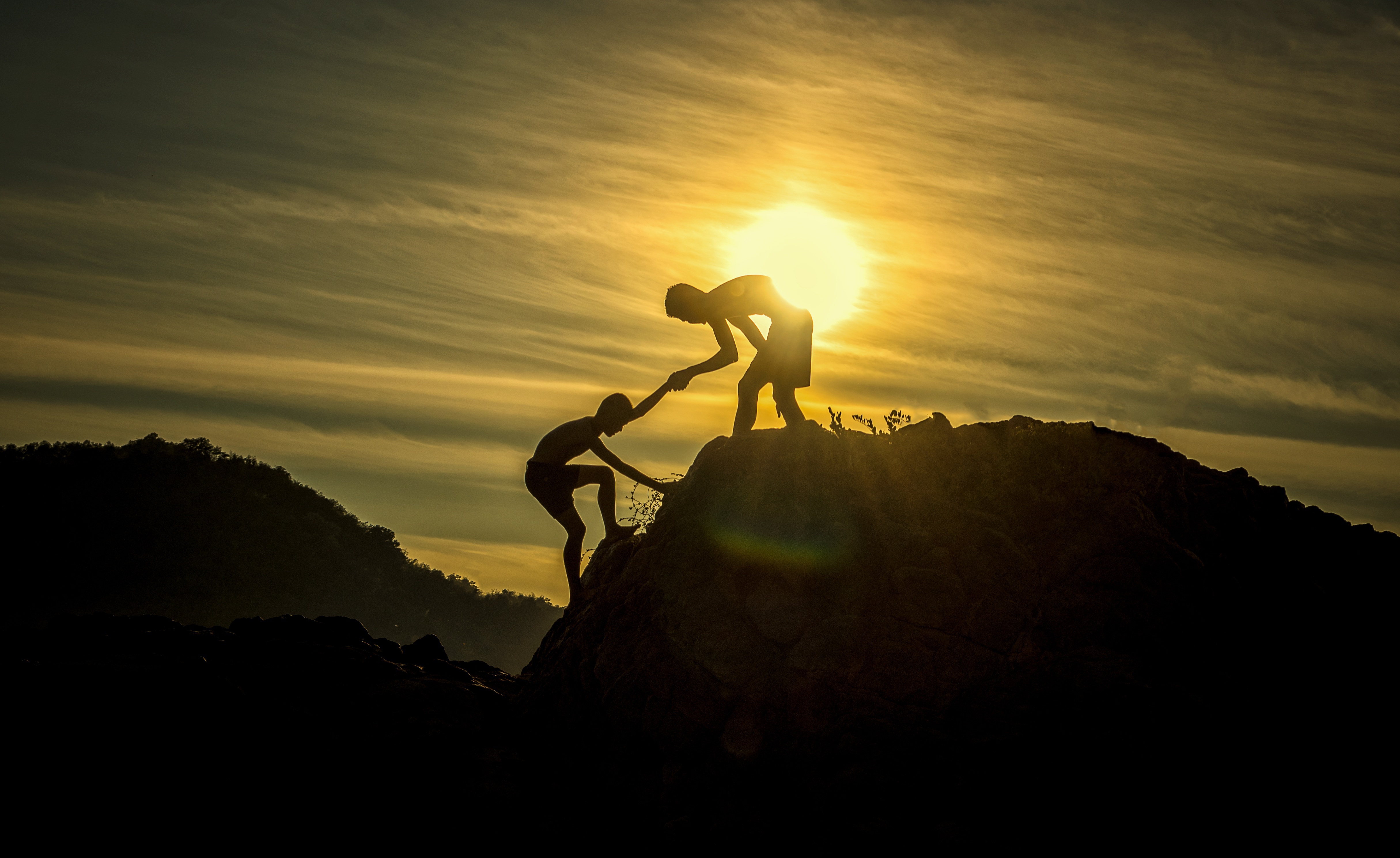 Two young adults support each other on a hike at sunset